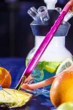 Nargile şişesi yuvarlak ve şeffaf, mavi likörle dolu. Dilimlenmiş portakal ve nane yaprakları likörde yüzer..