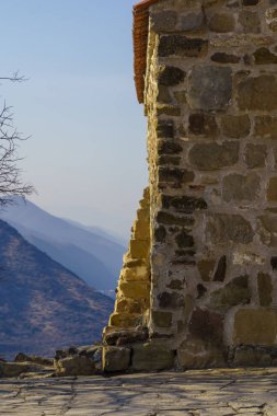 Eski duvar, binanın köşesi, kumdan ve gri taşlardan yapılmış. Dağın arka planında, Kafkaslar..