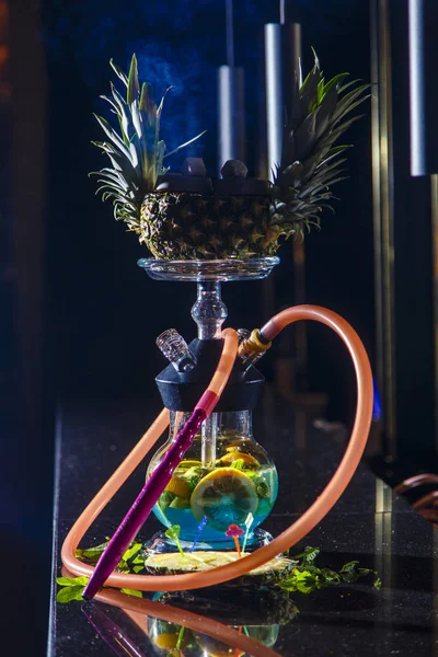 Hookah和一碗菠萝做的 胡卡酒瓶圆圆的，透明的，充满蓝绿色的酒。 切碎的橙子和薄荷叶漂浮在酒中. 很多烟. — 图库照片