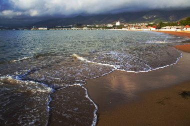 Gün batımında Gelendzhik kumsalında küçük dalgalar kırılır. Ve arka planda, bulutlardaki dağlar..