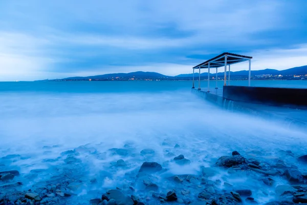 Fırtına dalgaları yüksek hızda Gelendzhik sahilinin taşlarını aşıyor. Maruz kalma nedeniyle dalgalar mavi bir sis. Gelendzhik tatil köyü, akşam alacakaranlığı.. — Stok fotoğraf