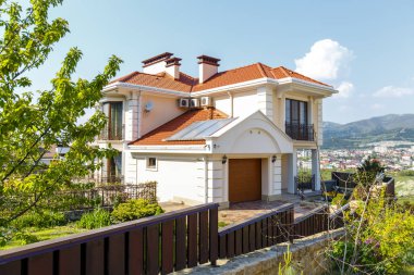 Klasik Akdeniz tarzı beyaz ve şeftali rengi, kırmızı kiremit çatılı üç katlı kır evi. Baharda dağların arka planına karşı. Yaşam tarzı. Gerçeklik