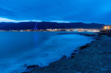Fırtınada Gelendzhik plajı. Mavi tonlar. Yüksek hızdaki dalgalar mavi bir sise dönüşür. Çakıl taşı plajı, dalgakıran. Arka planda, Kafkas dağları. 