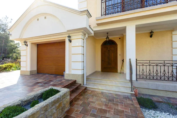La fachada de una casa de campo clásica blanca de dos pisos con jardín delantero. Puerta de entrada tallada, portón del coche, azulejos beige . — Foto de Stock