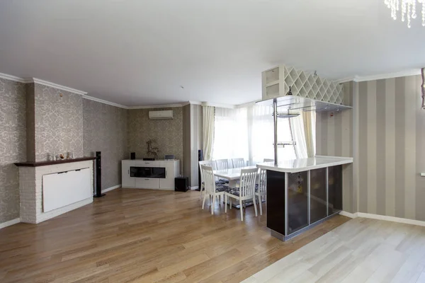 Large kitchen-living room in classic style and beige houses in the cottage. Black and white kitchen, beige Wallpaper with a pattern, bar counter, white table with chairs