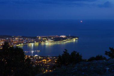 Akşam alacakaranlıkta Gelendzhik Körfezi, Kalın Burun ve Gelendzhik deniz feneri kuş bakışı. Sahilin ışıkları körfeze yansıyor..