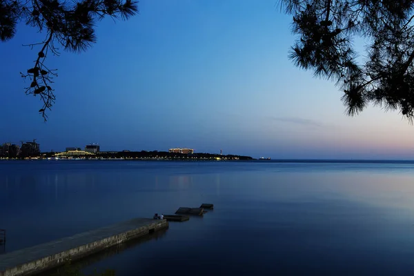 V zálivu Gelendzhik za soumraku. Klid. obloha modrá. V pozadí, maják Gelendzhik. světla promenády, hotelů a resortů — Stock fotografie