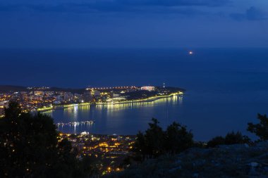 Akşam alacakaranlıkta Gelendzhik Körfezi, Kalın Burun ve Gelendzhik deniz feneri kuş bakışı. Sahilin ışıkları körfeze yansıyor..