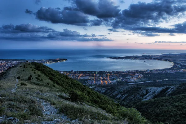 Gelendzhik Bay vanuit vogelperspectief. foto bij zonsondergang. Kaukasus bergen op de voorgrond. verlichte straten van de stad. donkerblauwe lucht, mooie donkere wolken — Stockfoto