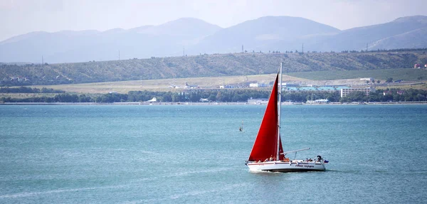 a yacht with scarlet sails sails along the Gelendzhik Bay on the background of the Caucasus mountains - a clear Sunny day