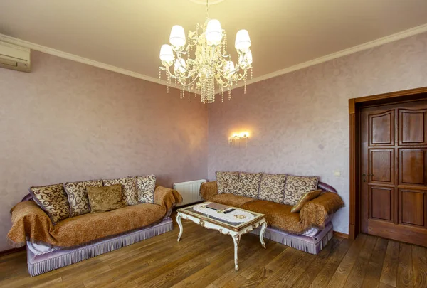 Twee gezellige beige banken met bruine strepen in de hoek van de kamer. voor hen staat een witte salontafel met gebogen poten — Stockfoto