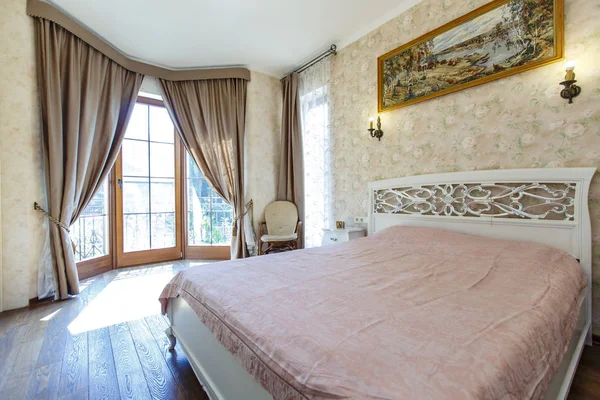 Camera da letto con una grande finestra dove splende il sole e un grande letto bianco con un copriletto rosa e uno schienale ricurvo fantasia — Foto Stock