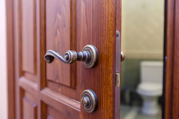 La puerta del baño se abre. Se abre una costosa puerta de caoba con asa vintage. Visible el inodoro . —  Fotos de Stock