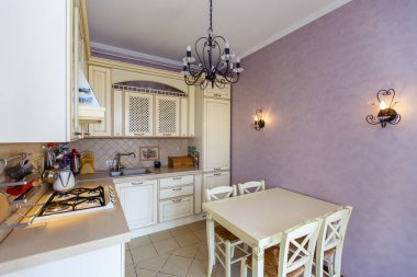 Provence tarzında küçük, rahat bir mutfak. Bej mobilyalar, sandalyeli masa, pembe duvarlar.