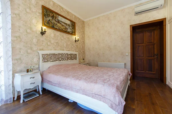 Una camera da letto in stile Provenza. Un grande letto bianco con gambe curve e schienale e un copriletto rosa. Carta da parati giallastra con un modello . — Foto Stock