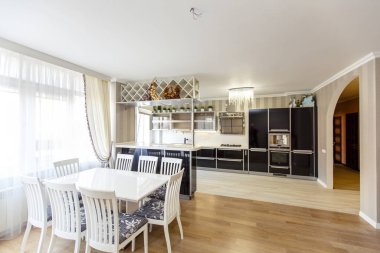 Mutfak ve yemek alanı olan yazlık evde büyük bir mutfak odası var. Lüks bir şekilde. Mutfak siyah beyaz, yemek masası ve sandalyeler beyaz.. 