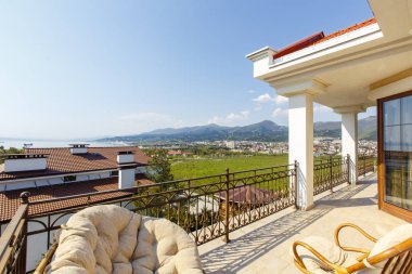 Kulübede dağ ve deniz manzaralı güzel, zengin, geniş bir veranda. Yumuşak hasır kanepeler ve koltuklar. Güzel beyaz fayansları olan bir veranda.. 