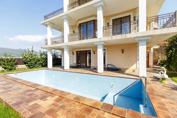 El patio trasero de una cabaña blanca de tres pisos con columnas. Jardín verde, césped y piscina vacía frente a la casa . — Foto de Stock