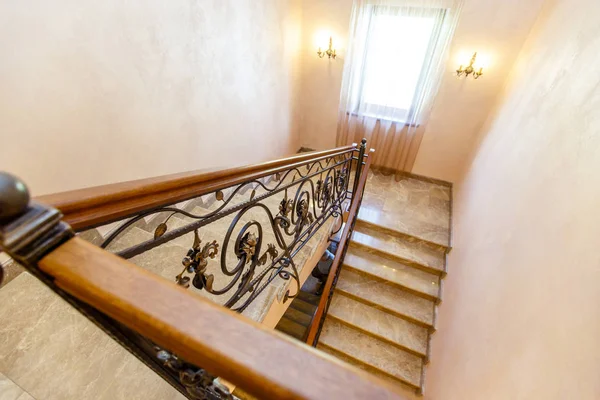 wrought iron staircase in the cottage. Marble steps, black wrought iron stairs with floral ornaments. Mahogany wooden railing.