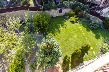 Kulübenin arka bahçesinde yeşil çimenli çimenler. Kulübenin beyaz duvarları, sütunlar, ağaçlar. Sulu bahar yeşillikleri. Laksheri.