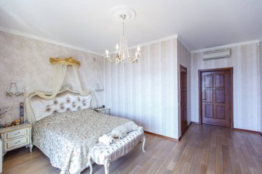 Büyük, çift kişilik yataklı, zarif, beyaz bir yatak odası. Beyaz sırtlı, küçük, kıvrımlı bacaklı beyaz komodinli. Açık çizgili duvar kağıdı. Mumlar için lambalar ve avize.