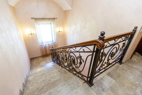 wrought iron staircase in the cottage. Marble steps, black wrought iron stairs with floral ornaments. Mahogany wooden railing.