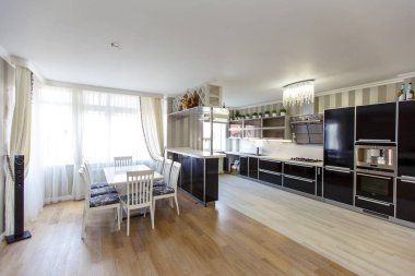 Klasik tarzda büyük mutfak oturma odası ve yazlıktaki bej evler. Siyah beyaz mutfak, desenli bej duvar kağıdı, tezgah, sandalyeli beyaz masa.