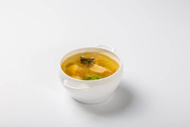 Somonlu balık çorbası. Beyaz yuvarlak bir tabak, somon, patates ve yeşillik parçaları gösteren şeffaf bir et suyuyla doludur. Beyaz arka planda bir plaka. Yan görünüm