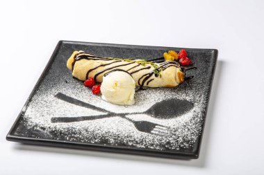 Meyveli bisküvi, içinde dondurma ve ahududu olan siyah bir tabakta yatıyor. Beyaz arkaplanda