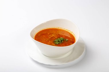 Dilli gulaş çorbası. Kırmızı çorbalı beyaz oval bir tabak beyaz arka planda duruyor.