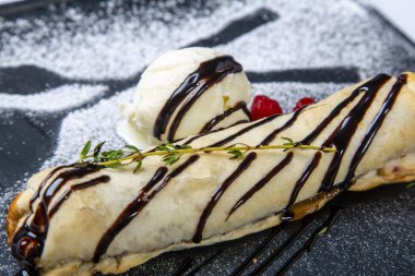 Meyveli bisküvi, içinde dondurma ve ahududu olan siyah bir tabakta yatıyor. Gri bir tuvalde. Yakın çekim görünümü