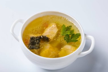 Somonlu balık çorbası. Beyaz yuvarlak bir tabak, somon, patates ve yeşillik parçaları gösteren şeffaf bir et suyuyla doludur. Beyaz arka planda bir plaka. Yukarıdan görünüşü