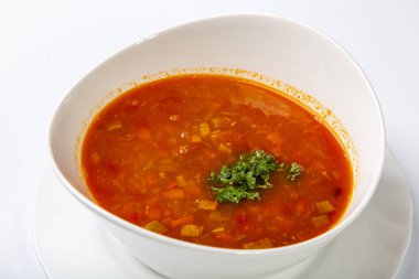 Dilli gulaş çorbası. Kırmızı çorbalı beyaz oval bir tabak beyaz arka planda duruyor.
