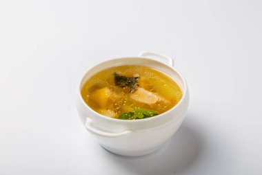 Somonlu balık çorbası. Beyaz yuvarlak bir tabak, somon, patates ve yeşillik parçaları gösteren şeffaf bir et suyuyla doludur. Beyaz arkaplan üzerine plaka. 