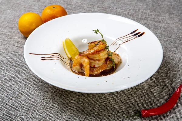 Smažené tygří ocásky s teriyaki omáčkou. Talíř na šedém plátně, vedle citrónů a chilli papriček — Stock fotografie