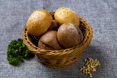 Beyaz ve çavdar ekmekli hasır ekmek sepeti. Gri bir tuvalde. Ekmek sepetinin yanında tohum ve maydanoz var..