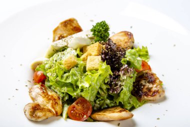 Caesar salad with chicken and feta cheese.  Served on a round white plate: pieces of fried chicken, cheese, tomatoes, salad.  Close up