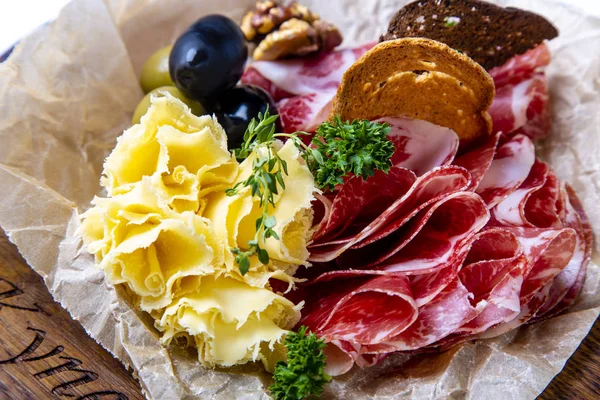 Em uma tela cinza, cercada por vegetação e nozes, há conjuntos de vinhos: pescoço seco, queijo, azeitonas e biscoitos de centeio. Seth está deitado em papel manteiga em uma bandeja de madeira redonda . — Fotografia de Stock