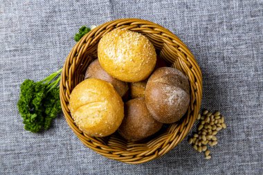 Beyaz ve çavdar ekmekli hasır ekmek sepeti. Gri bir tuvalde. Ekmek sepetinin yanında tohum ve maydanoz var..