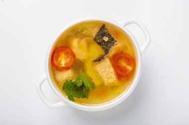 Somonlu balık çorbası. Beyaz yuvarlak bir tabak, somon, patates ve yeşillik parçaları gösteren şeffaf bir et suyuyla doludur. Beyaz arka planda bir plaka. Yukarıdan görünüşü