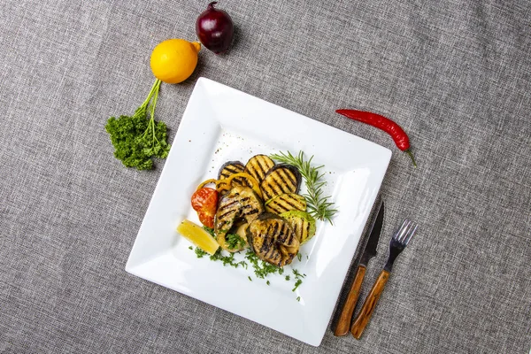 Bistecca di storione con verdure. Deliziose bistecche di storione vengono grigliate e servite su un piatto quadrato bianco con limone e pomodoro. Il piatto è su una tela grigia. La vista dall'alto — Foto Stock