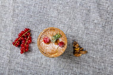 Şeffaf bardakta panna cotta tatlısı, üstünde kiraz ve nane ile süslenmiş. Gri bir tuvalde kırmızı fındık ve fındıkların yanında bir bardak. Yukarıdan görünüşü