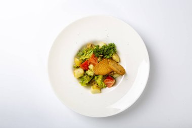 Sezar tavuklu ve peynirli. Yuvarlak beyaz tabakta servis ediliyor: kızarmış tavuk, peynir, domates, salata. Beyaz arkaplan üzerine plaka.