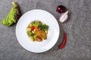 Ballı Rapan soslu, Karadeniz kıyılı bir salata. Çavdar krakerleriyle. Gri bir bez üzerinde, salatanın yanında, soğan başı, kırmızı biber.