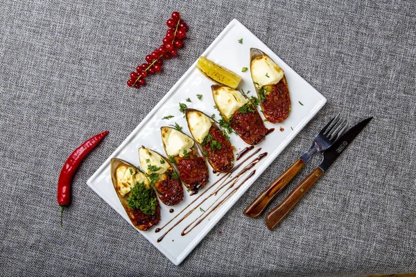 Mussels "saganaki". Mussels with feta cheese and spicy vegetables, fried in the oven. A mussels "saganaki" on a Gray canvas, next to a knife, fork — Stock fotografie