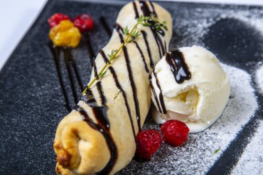 Meyveli bisküvi, içinde dondurma ve ahududu olan siyah bir tabakta yatıyor. Gri bir tuvalde. Yakın çekim görünümü