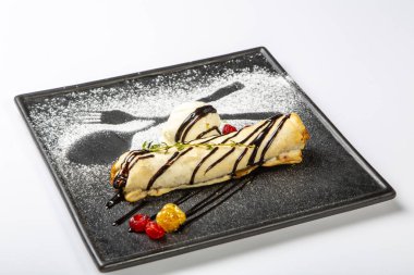 Meyveli bisküvi, içinde dondurma ve ahududu olan siyah bir tabakta yatıyor. Beyaz arkaplanda