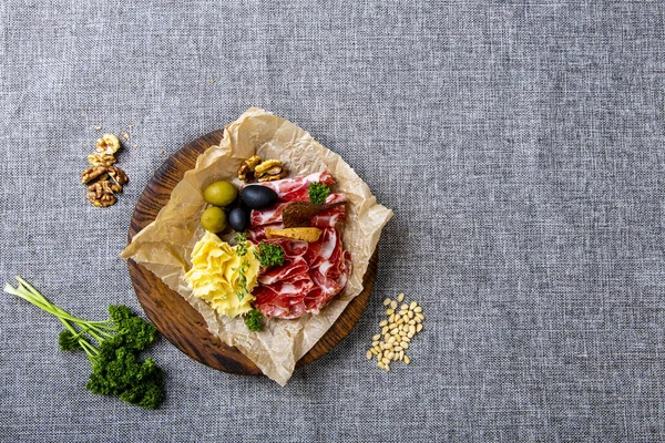 En un lienzo gris, rodeado de vegetación y frutos secos, hay conjuntos de vino: cuello seco, queso, aceitunas y galletas de centeno. Seth está acostado sobre papel de pergamino arrugado en un tra redondo de madera —  Fotos de Stock