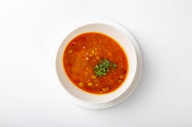 Dilli gulaş çorbası. Beyaz arka planda kırmızı çorbalı beyaz bir oval tabak duruyor. Yukarıdan görünüşü