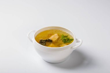 Somonlu balık çorbası. Beyaz yuvarlak bir tabak, somon, patates ve yeşillik parçaları gösteren şeffaf bir et suyuyla doludur. Beyaz arka planda bir plaka. Yan görünüm